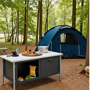 Camp table with a white top and dark cabinet set up beside a blue tent in the woods