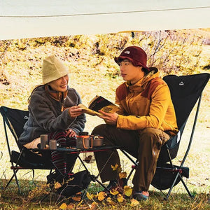 Two friends in black folding camping chairs at camp