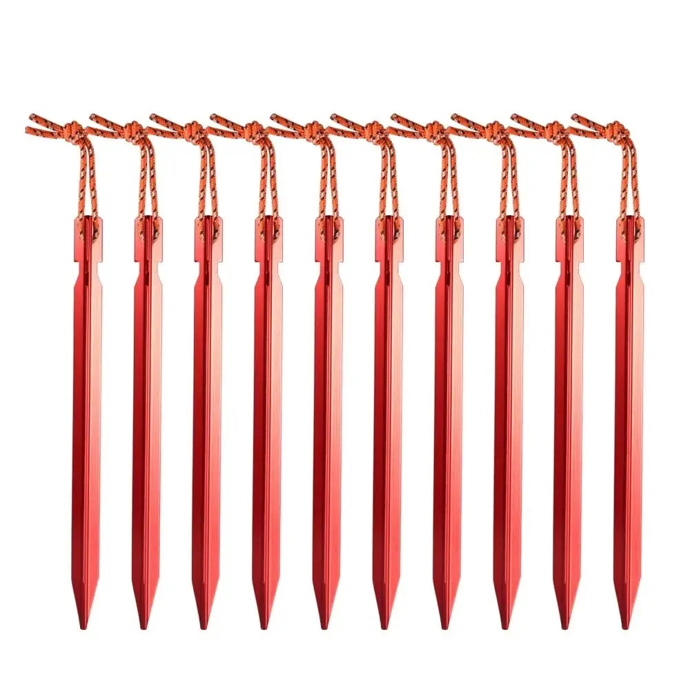 Red TriPeg Y-beam tent stake driven into rocky ground holding a tent guy line, two more stakes on a rock, mountains behind