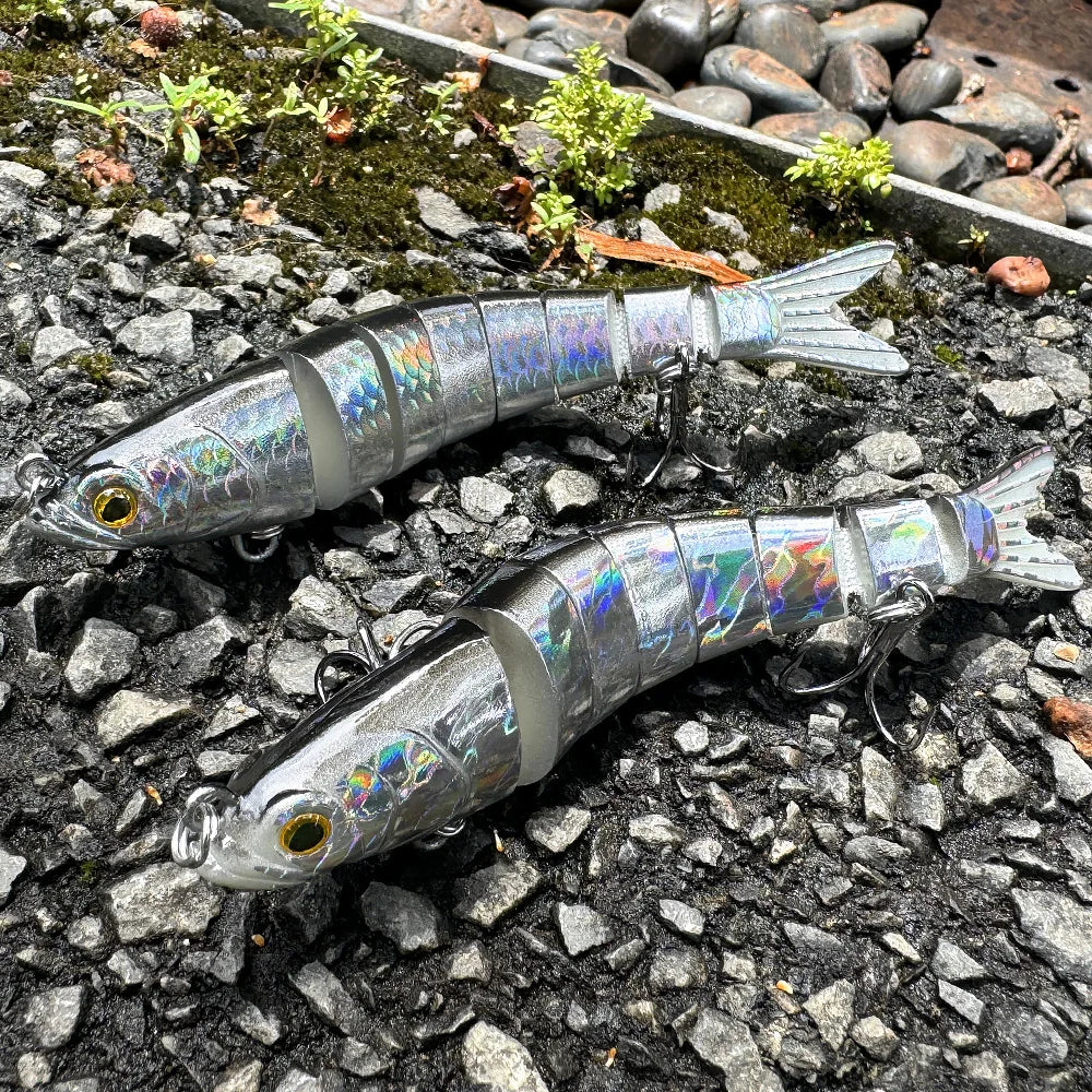 Two silver jointed swimbait lures with treble hooks on wet gravel