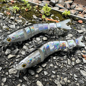 Two silver jointed swimbait lures with treble hooks on wet gravel