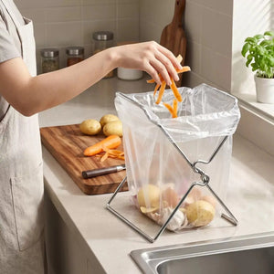 Cook drops carrot peels into a bag on a steel holder beside the cutting board
