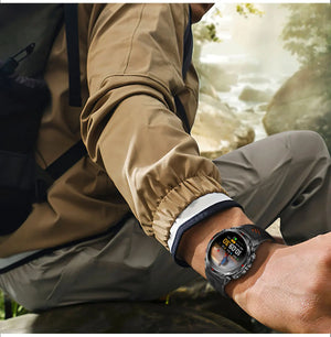 Hiker in tan jacket wearing a black smartwatch with orange-striped band, seated by a forest stream