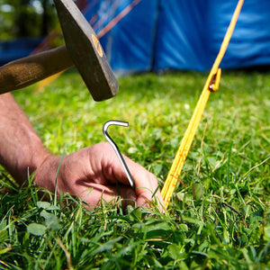 Mallet tapping a hook stake into grass over a yellow tent rope