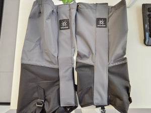 Two gray and black gaiters laid flat, logo patch on each front strip