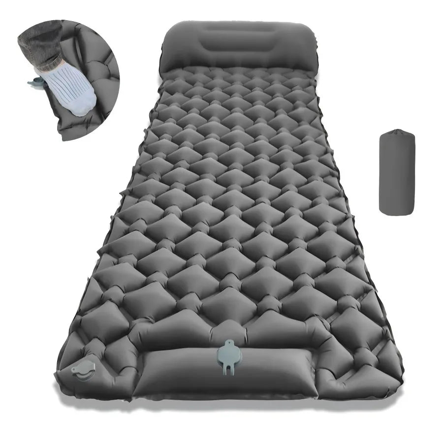 Gray CampCloud air pad with built-in pillow laid out by a tent while a hiker laces his boots at a forest campsite