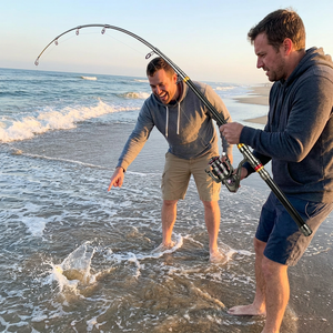 Two friends surf fishing on the beach with a telescopic rod and reel combo bent with a fish on