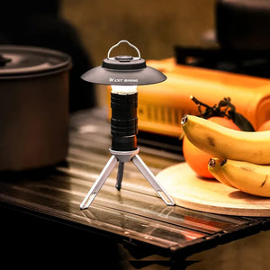 Black mini camping lantern with a round shade on a small tripod, on a camp table by fruit