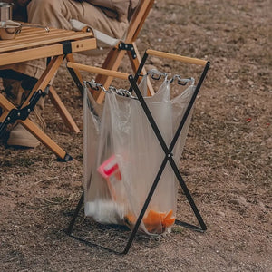Black TidyBin Pro stand at a campsite holding a clear trash bag open by its handles