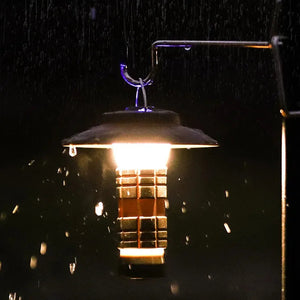 Mini lantern glowing warm while hanging from a metal hook in the rain at night