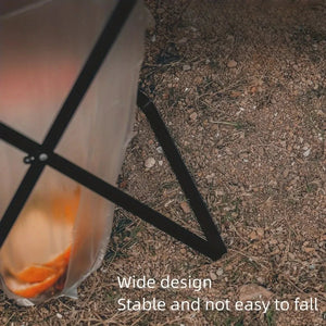 Close-up of the trash bag stand's wide X-frame legs on gravel, with a full bag