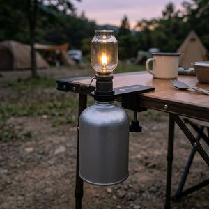Matte black gas canister table mount clamped to a camp table holding a glowing lantern at dusk