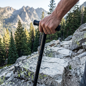 Hand on the T-handle of a black survival trekking staff on a rocky mountain trail