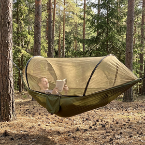 Person reading inside a green hammock with a zipped mosquito net between pine trees