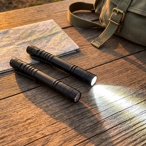 Two PenBeam black pen lights on a wooden camp table beside a map, one switched on