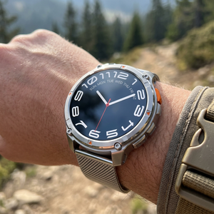 TrailCore outdoor smartwatch with a silver mesh band on a wrist near a mountain trail