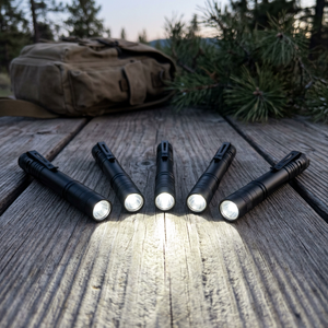 Five PenBeam black pen lights fanned out on a wooden camp table at dusk, all five switched on