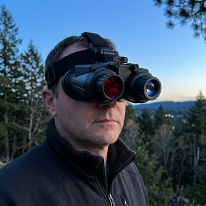 Man wearing NightHawk 3D head-mounted night vision goggles on a forest ridge at dusk