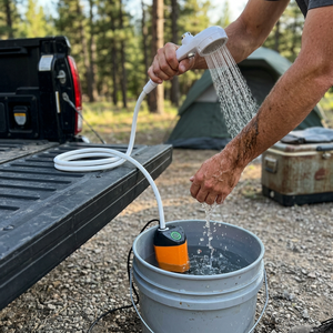 TrailRinse shower pump in a bucket of water; a man rinses mud off his arm with the hand shower by a truck