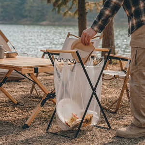 Black TidyBin Pro folding trash bag holder beside a camp table at a lakeside campsite