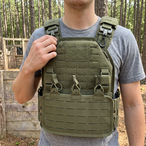 Player at an outdoor airsoft field wearing an army green plate carrier style vest