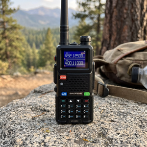 Black SkyCopy two-way radio standing on a granite rock beside a hiking trail, backpack behind it, pine valley in the distance