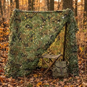 StealthShield woodland camo net draped over a pole frame as a hunting blind in an autumn forest, stool and pack inside