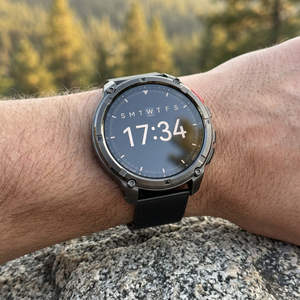 TrailCore outdoor smartwatch with a black mesh band on a wrist at a trail overlook at golden hour