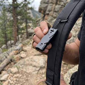 Hiker holding the Steel Black TrailCall dual-tube survival whistle clipped to a backpack strap
