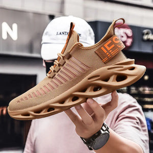 Tan TrailHawk running shoe with an orange heel tab, held up in one hand on a city street